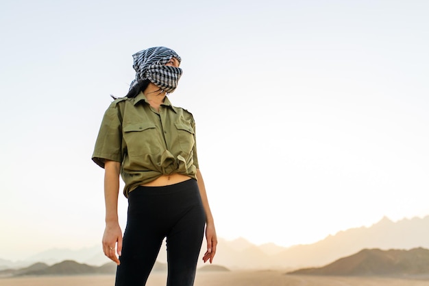 Donna con la testa e il viso coperti con sciarpa a scacchi bianca e nera in piedi sullo sfondo del deserto