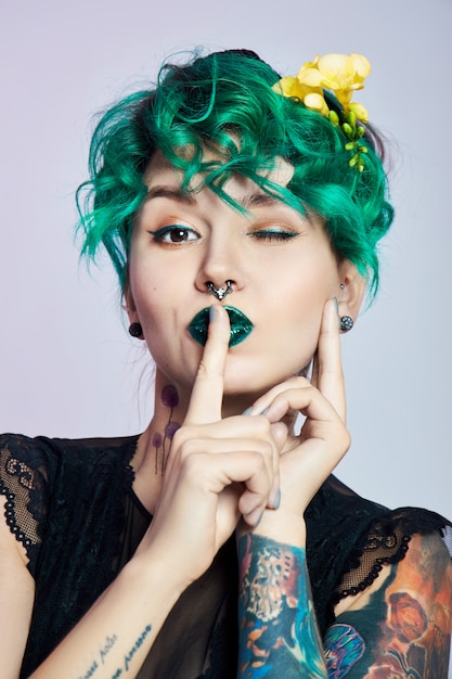 Woman with creative green coloring hair and makeup, toxic strands of hair. Bright color curly hair on the girl head, professional makeup. Woman with tattoo