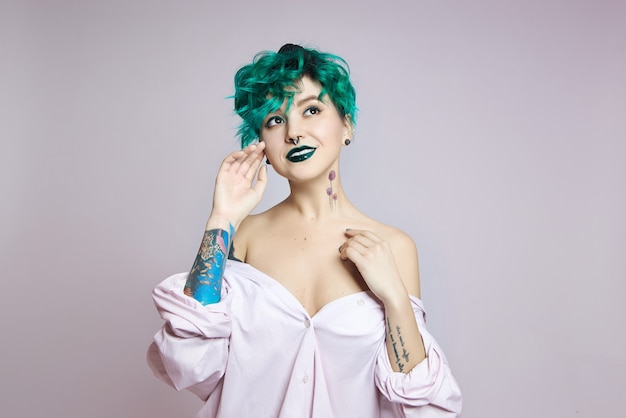 Woman with creative green coloring hair and makeup, toxic strands of hair. Bright color curly hair on the girl head, professional makeup. Woman with tattoo