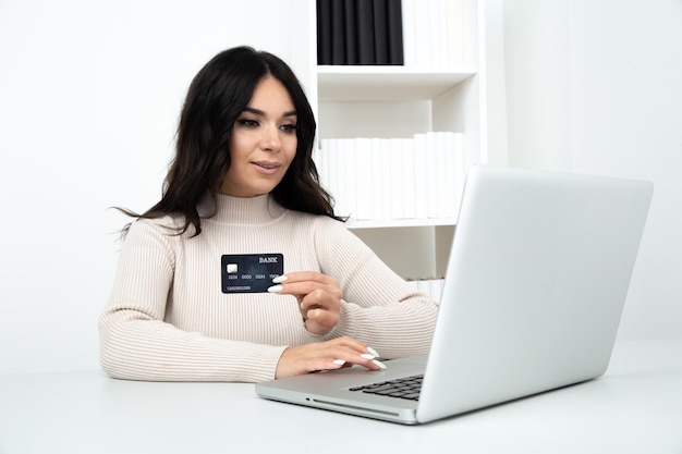 Женщина с кредитной картой делает оплату онлайн, сидя в изолированном офисе