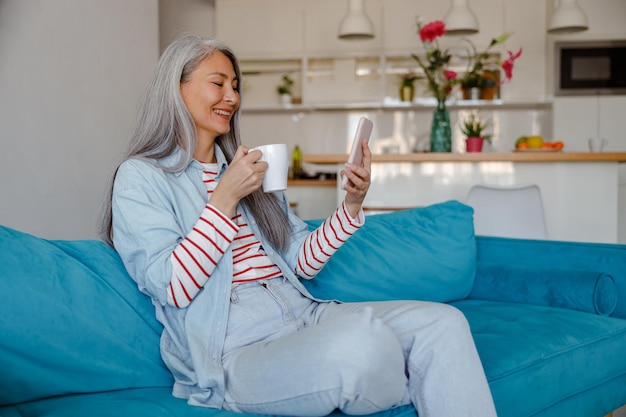 Woman with cup of coffee using cellphone at home