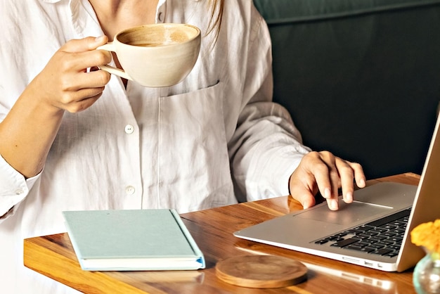 Photo woman with a cup of coffee working at laptop face unrecognized