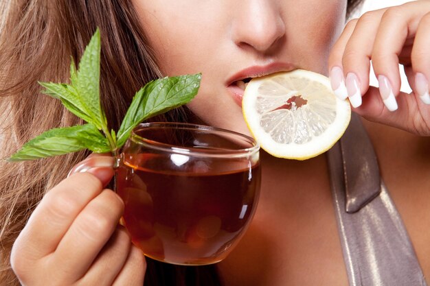 Woman with cup of fresh tasty black tea, mint and lemon