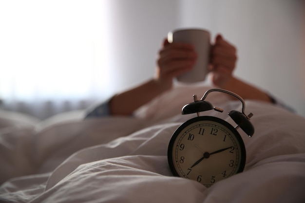 Фото Женщина с чашечкой в постели сосредотачивается на будильнике утром