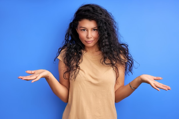 Woman with curly black hair shrugging misunderstanding, portrait of emotional female isolated