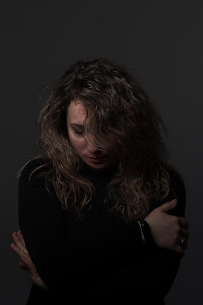 a woman with curly hair on a dark background lowered her head, a woman over 30 years old