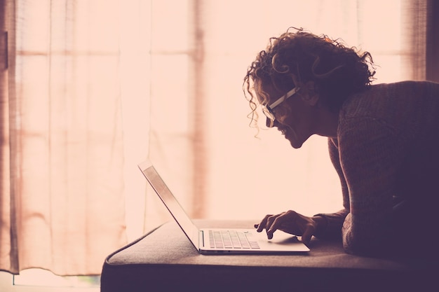 woman with curly hair and eyeglasses working with laptop computer comfortably sitting on sofa at home