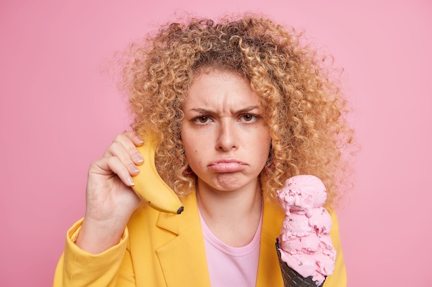 woman with curly hair holds banana near ear pretends calling someone eats ice cream expresses negative emotions 