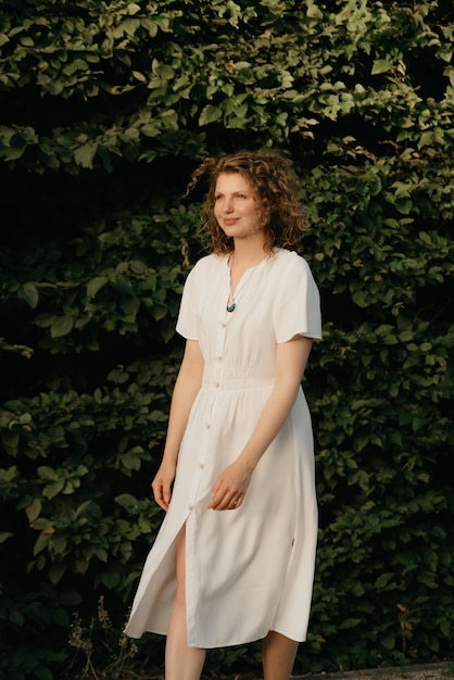 A woman with curly hair is posing in the garden in the evening