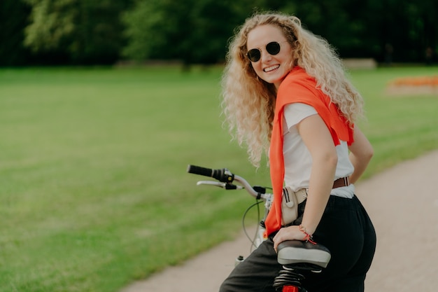 Woman with curly hair, looks from back, stops during riding bicycle