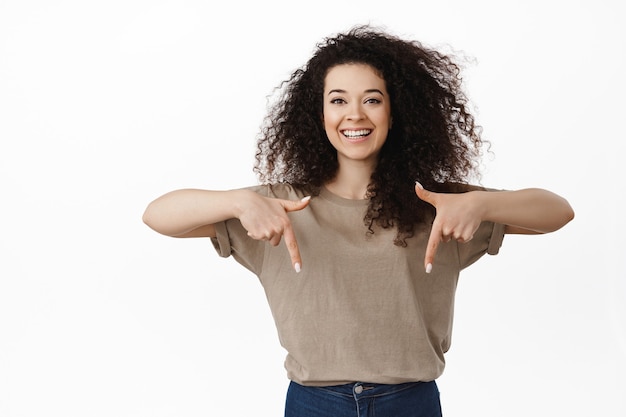 woman with curly hair pointing fingers down, showing sale copy spaceon white