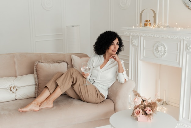 Woman with curly hair and a snow-white smile sits on the sofa and looks away