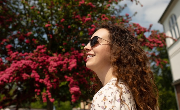 A woman with curly hair stands in front of a flowering tree.