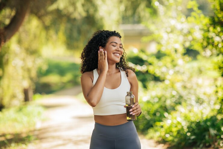 Photo a woman with curly hair stands in a sunlit park smiling and holding a water bottle she appears to be