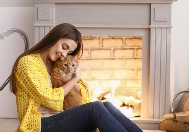 Woman with cute cat resting near fireplace