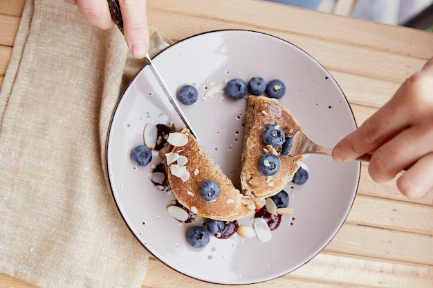 Woman with cutlery eating traditional pancakes with fresh blueberries and agave syrup on a plate Breakfast outside on the terrace