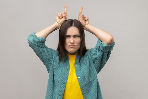 Woman with dark hair showing bull horns gesture over head frowning as before attack