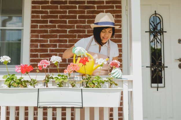 写真 屋外で鉢植えのゼラニウムに水をやる黒髪の女性