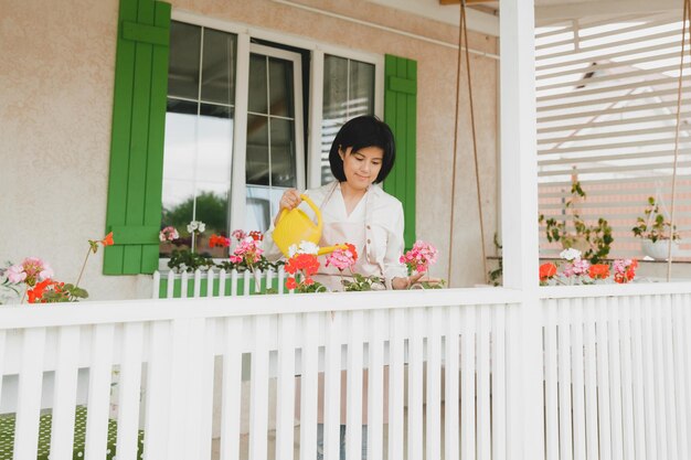 Woman with dark hair watering potted plants geraniums outdoors