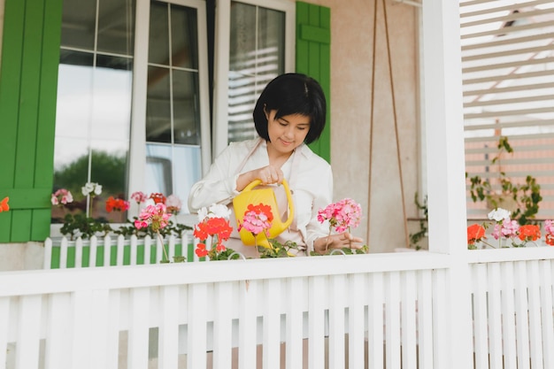 Woman with dark hair watering potted plants geraniums outdoors