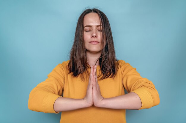 Woman with dark straight hair holds arms folded in front of chest Meditation Blue background