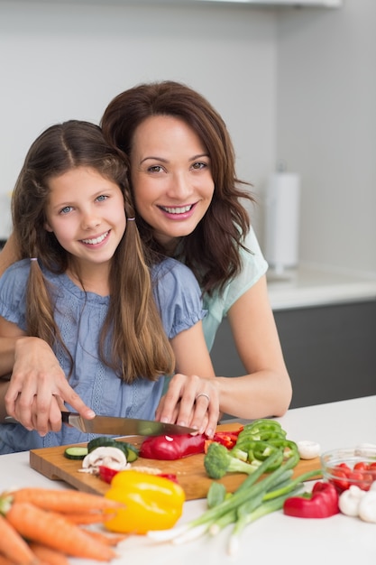 Donna con la figlia che taglia le verdure a pezzi in cucina