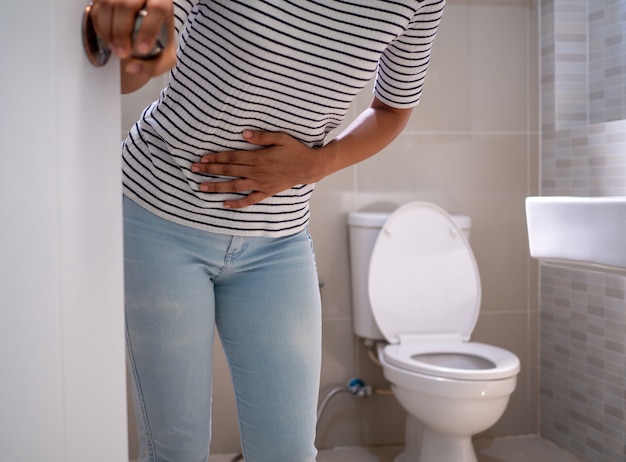 Foto donna con diarrea in piedi nel bagno, tenendo il suo stomaco. grave mal di stomaco, preparati a sederti sterco in bagno