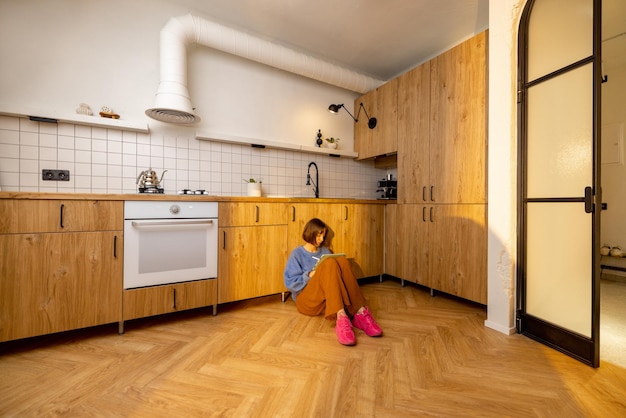 Женщина с цифровым планшетом сидит на кухонном полу