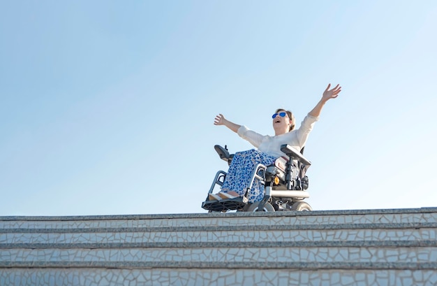 Woman with a disability screaming excited while sitting with open arms in wheelchair at top of stairs