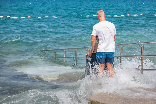 Woman with disability on wheelchair at accessible beach goes swimming