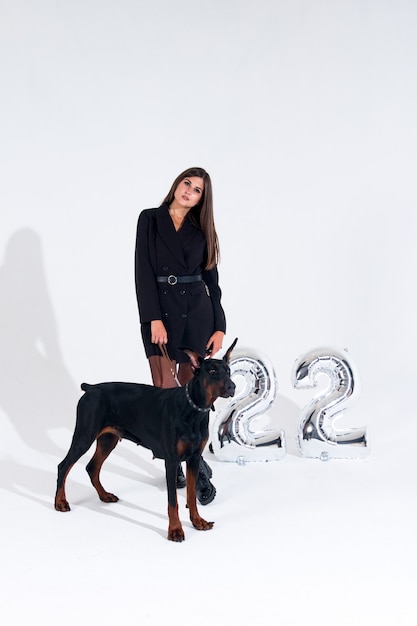 Photo a woman with a doberman black dress on a white background. a woman trains a pet