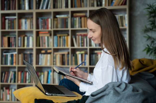 Woman with documents using a laptop at home against rack of books