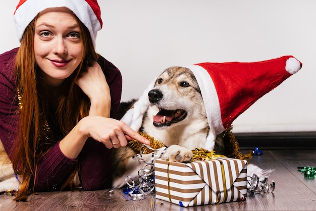 クリスマスの帽子をかぶった犬を持つ女性は、贈り物の背景にあります