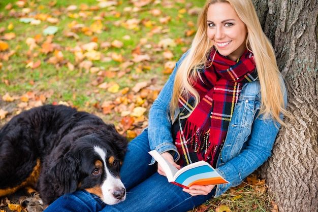 Woman with dog reading book in autumn park