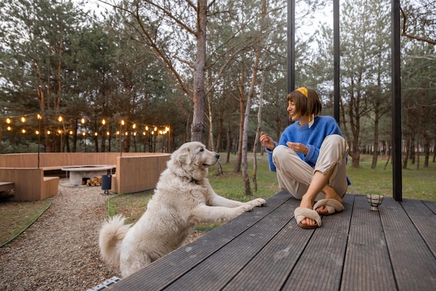 Woman with dog rests near wooden cottage in nature