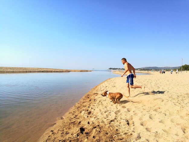 Woman with dog running on beach against clear sky