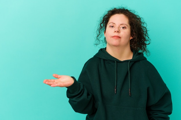 Photo woman with down syndrome isolated showing a copy space on a palm and holding another hand on waist