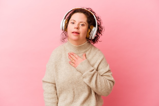 Фото Женщина с синдромом дауна с наушниками, изолированными на розовом фоне, громко смеется, держа руку на груди.