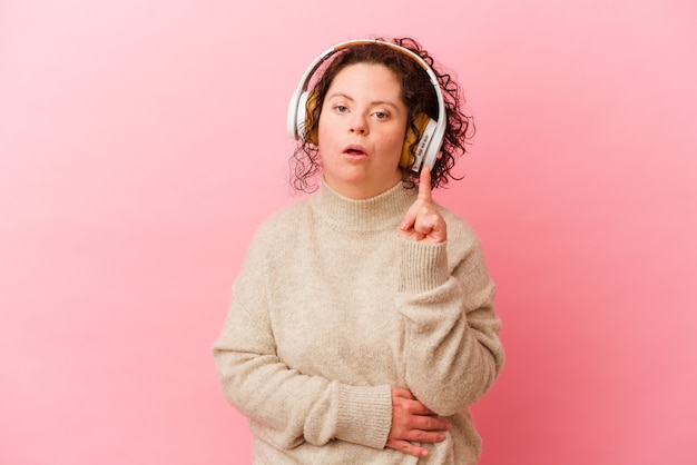 いくつかの素晴らしいアイデアを持っているピンクの壁に分離されたヘッドフォンでダウン症の女性。創造性の概念