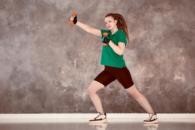 아령을 든 여자가 체육관에서 훈련하는 동안 권투를 하고 있다