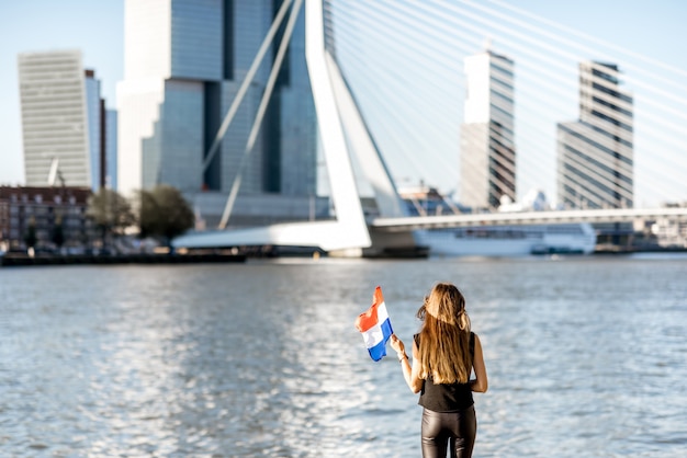 Woman with dutch flag enjoying beautiful cityscape view on the modern riverside during the morning in Rotterdam city