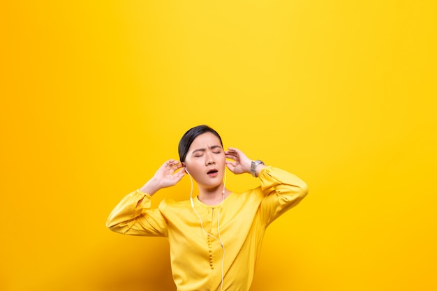 Woman with earphones listening music on isolated yellow wall