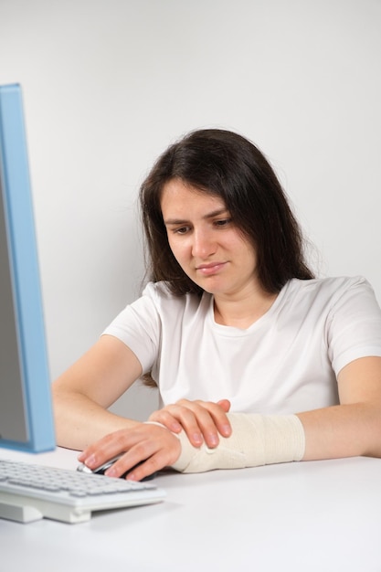 A woman with an elastic bandage on her wrist sits in front of a computer