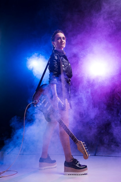 Woman with electric guitar on stage and smoke