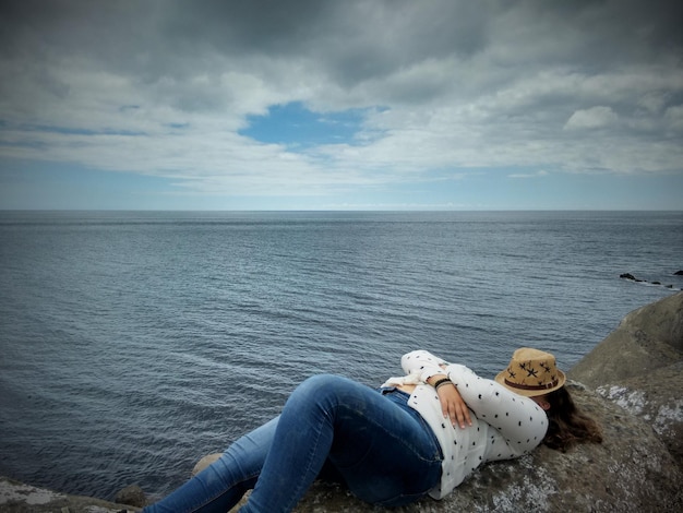 海の向こうの岩の上でリラックスする帽子で覆われた顔の女性