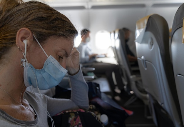 Woman with face mask and earphones sitting on plane. Airplane health measures concepts