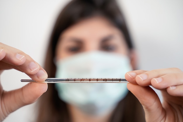 Photo woman with a face mask looking at a thermometer.