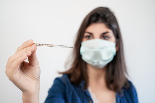 Photo woman with a face mask looking at a thermometer.