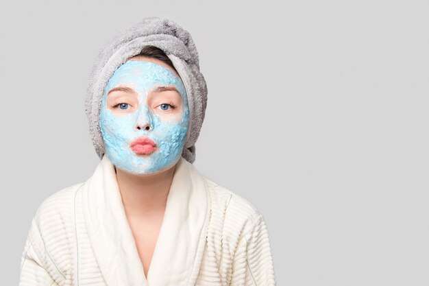 Woman with facial clay mask at spa salon or at home, skincare theme. Girl removes alginate cosmetic mask. Face mask, spa beauty treatment with copy space