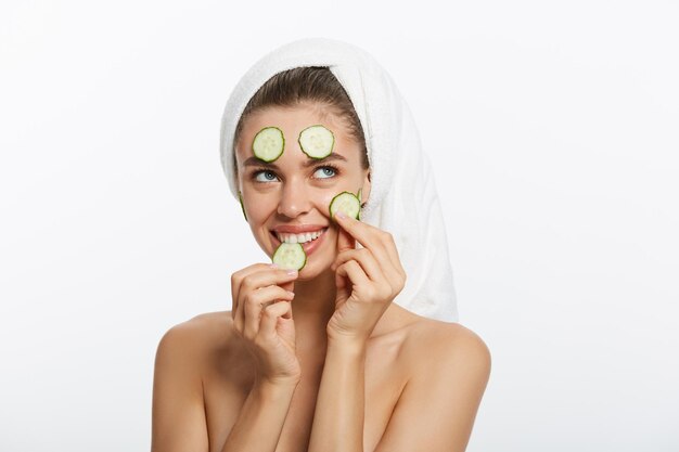 Woman with facial mask and cucumber slices in her hands on white background